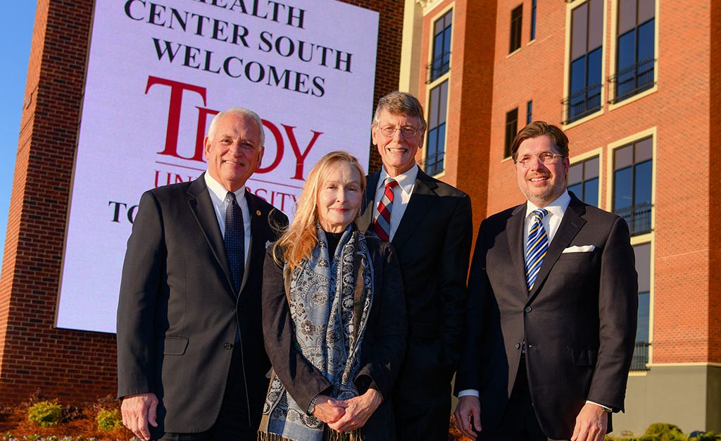 Four people standing in front of Troy welcome sign