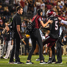 Athletic Trainers helping a football player off of the field.
