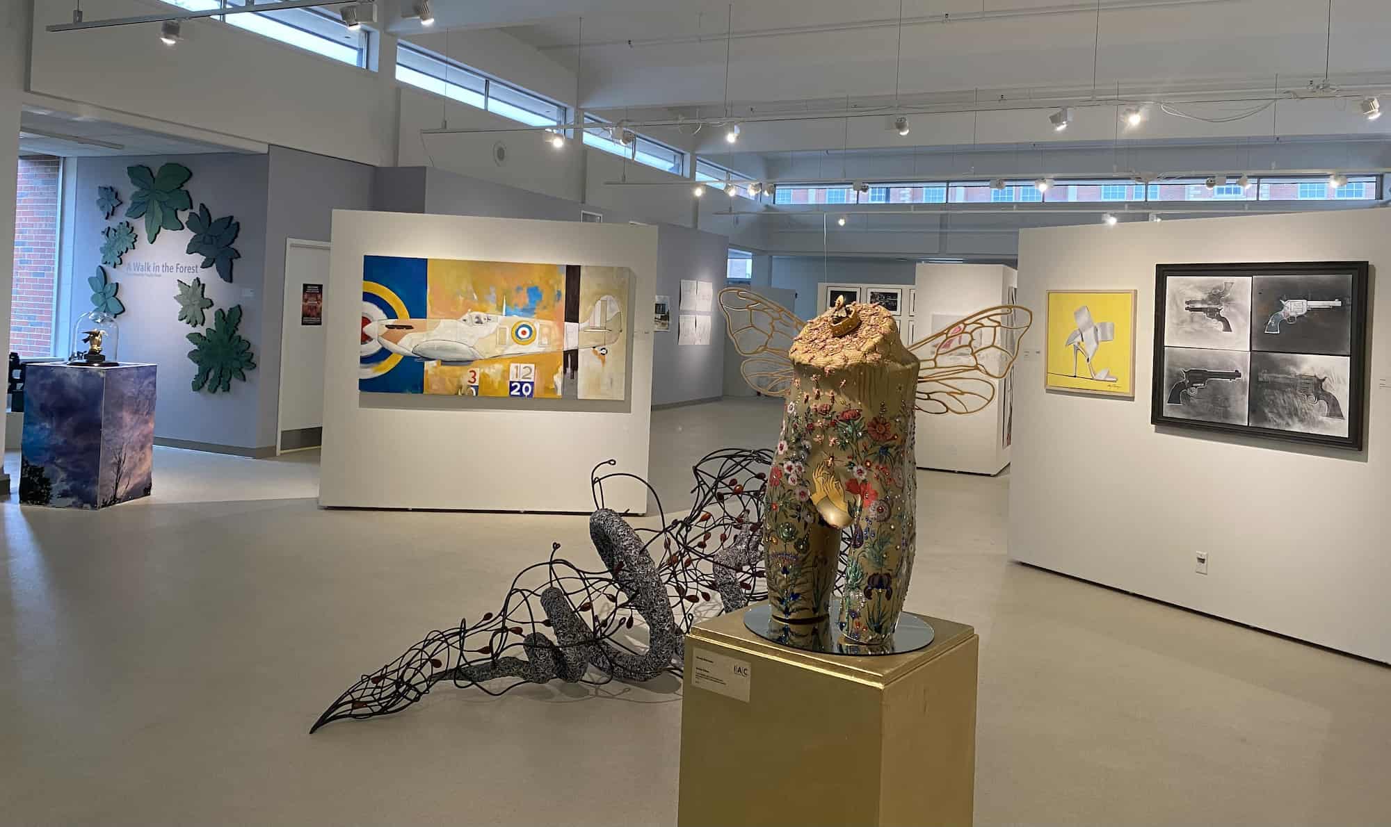 Image shows the entirity of the gallery featuring a painting of an airplane and a golden mannequin sculpture with bee wings.