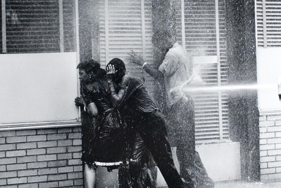 Three black adults are pushed against a wall by the shear force of the Alabama Fire Department's high pressure water hose in response to civil rights protests.