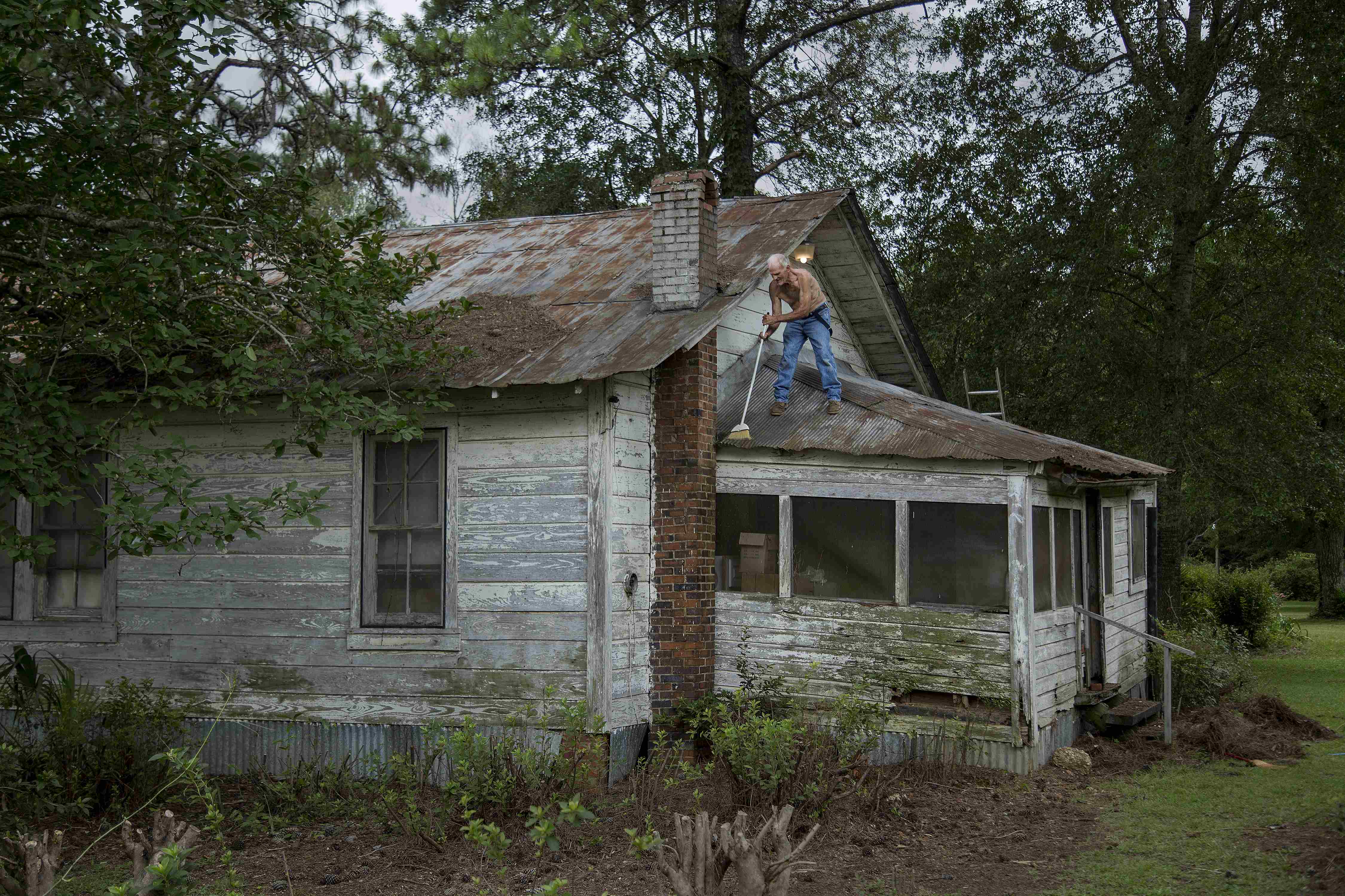 Elderly man standing on roof, sweeping off foliage.
