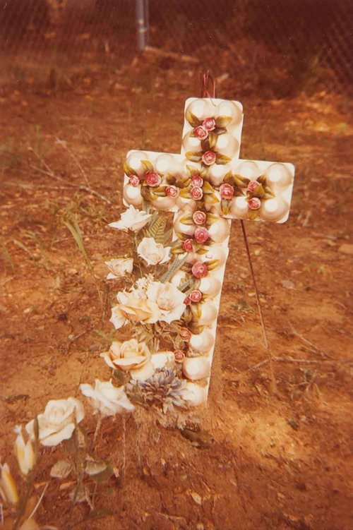 epia image of a dirt grave with a handmade egg carton cross decorated with roses.