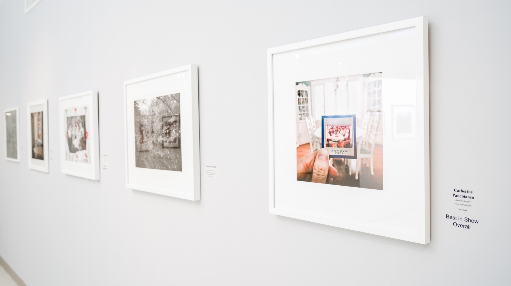 A perspective shot of several photos framed on a white wall. As the perspective goes further into the background, the images furthest away begin to blur with the background. 