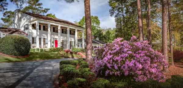 Pink azaleas and a beautifully landscaped lawn surrounds the driveway in front of the Chancellor’s two-story residence that is accented with six white columns and a red door. 