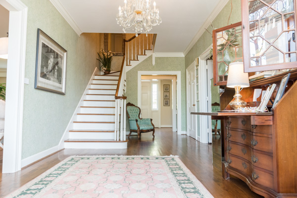 Looking from the front door, a beautiful staircase leads to the second floor, while a secretary’s desk, green and pink rug and chair decorate the hallway.