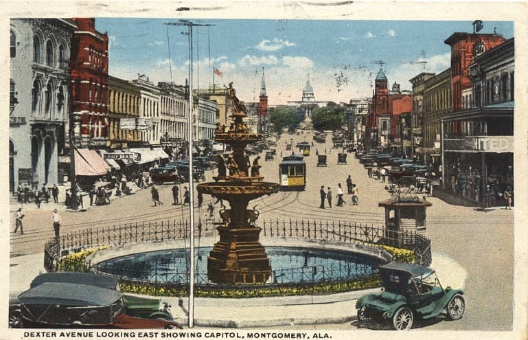 Color print of Dexter Avenue in Montgomery, Alabama showing the Court Square Fountain, multi-story commercial buildings, streetcars and rails, and the Alabama Capitol. Postmarked July 18, 1922.