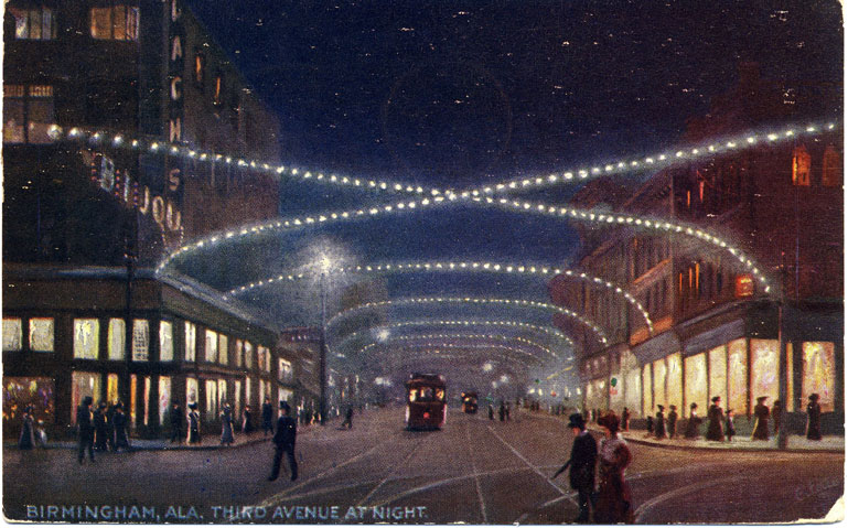 Color print of the business section of Third Avenue in Birmingham, Alabama at night with white lights stretched across street. Postmarked April 29, 1910.