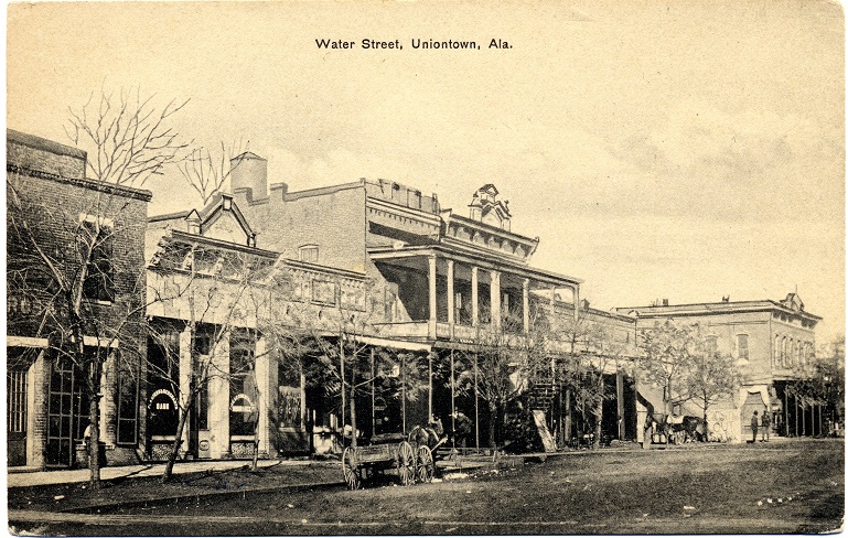 Black and white print of unpaved Water Street in Uniontown, Alabama showing one and two-story commercial buildings.