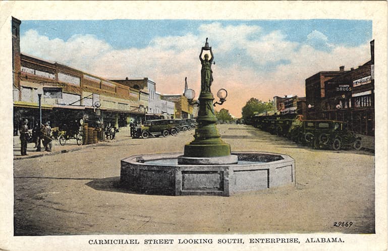 Color print of the Boll Weevil Monument and one and two story commercial buildings on Carmichael Street in Enterprise Alabama.
