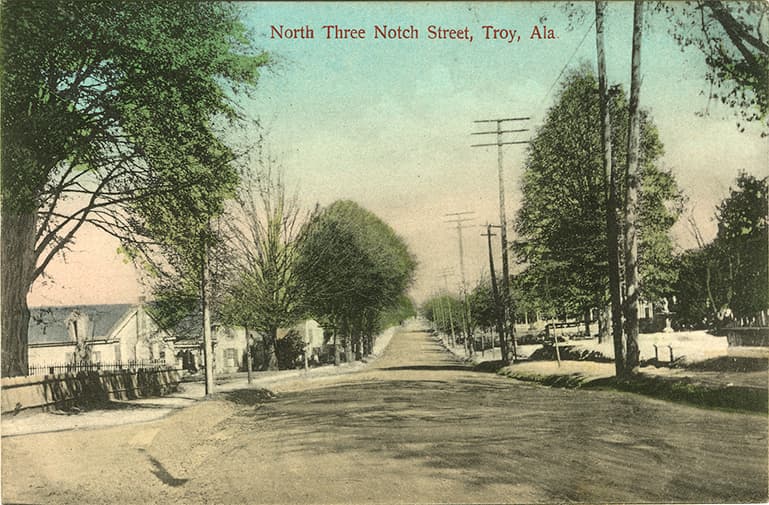 Mostly black and white photograph of residential section of unpaved North Three Notch Street in Troy, Alabama.